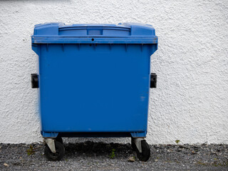 A blue trash can is sitting on the side of a road. The trash can is empty and has a white stripe on...