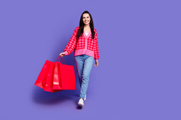 Full length photo of cheerful cute lady dressed pink cardigan holding bargains empty space isolated violet color background