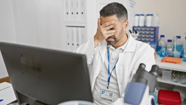 Baffled young hispanic man in scientist uniform doing a double-take, peeking via splayed fingers to cover face. the shock in his eyes screams 'wow' in the lab!