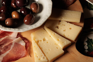 tagliere di legno con una scodella di olive nere, fette di formaggio e prosciutto crudo come...