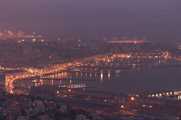 Fototapeta premium vista in primo piano di parte della città di Trieste nella zona centrale e del porto che si affaccia sul mare Adriatico e il golfo, visto dall'alto, di sera, con le luci delle strade accese