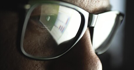 Close-up portrait in profile of part of the face. A young adult Caucasian man in a business suit and glasses with glasses reflecting the reflection of a laptop screen with news on a dark background