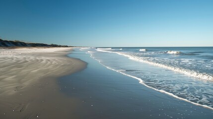 A serene beach with gentle waves lapping the shore, soft sand, and a clear blue sky