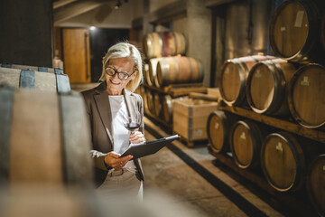 Mature senior woman stand in basement hold clipboard and glass of wine