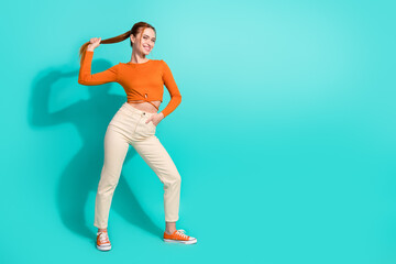 Full length photo of lovely cute woman wear orange crop top pants hand hold tail palm on waist isolated on turquoise color background