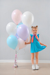 Cute little girl with beautiful balloons near grey wall