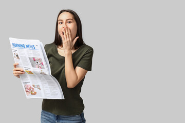 Shocked young woman with newspaper on grey background