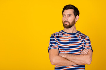 Portrait of handsome confident thoughtful businessman in striped t shirt crossed hands isolated on yellow color background