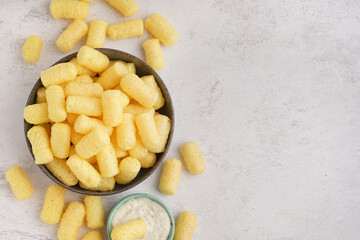 Bowl with tasty salty corn sticks and sauce on light background