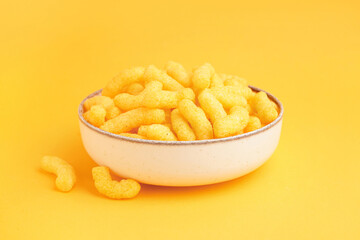 Bowl with tasty salty corn sticks on orange background