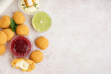 Paper with delicious fried mozzarella balls, lime and sauces on light background
