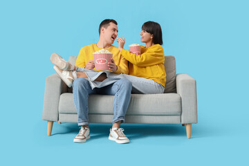 Young couple in love eating popcorn on sofa against blue background