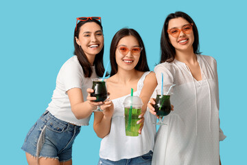 Happy young women with glasses of cocktail on blue background. Summer party