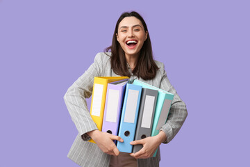 Happy young businesswoman with folders on lilac background