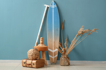 Surfboard with pampas grass, stool and bag near blue wall in room