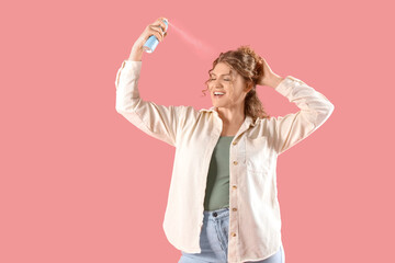 Young woman applying dry shampoo on her hair against pink background