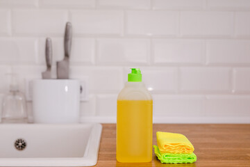 White plates, glass cups and forks in a clean white sink and two bottles of detergent and rags