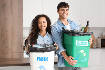 Young couple with garbage containers in kitchen. Waste sorting concept
