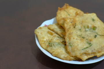 Tempe Mendoan in wahite plate and brown background, traditional fried tempeh, one of popular street food from Indonesia, food, stock photo.