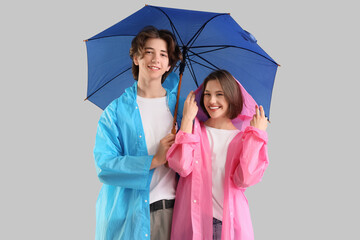 Young couple in raincoats with umbrella on light background