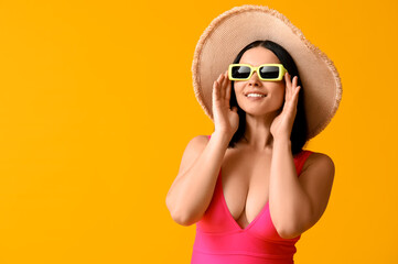 Beautiful young woman in stylish pink swimsuit and sunglasses on yellow background