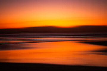 Stunning sunset over the ocean at Byron Bay, Australia, with vibrant orange and yellow hues reflecting on the calm water. 