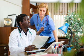 Portrait of two multinational doctors in the office of a resident of the clinic, sitting at a table...