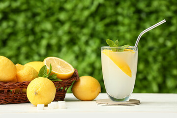 Glass of fresh lemonade with mint on white wooden table outdoors