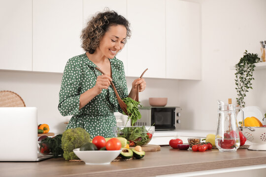 Mature woman stirring vegetable salad in kitchen