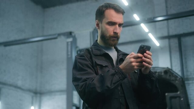 Male guy mechanic Caucasian adult man engineer technician industrial worker electrician in uniform using mobile phone think thoughtful typing smartphone app online order working in car service station - Powered by Adobe