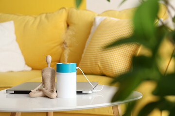 Air humidifier with statuette and laptop on table in living room, closeup