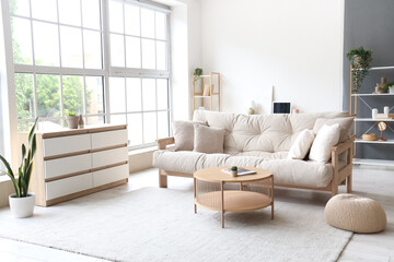 Interior of light living room with beige couch, table and big window