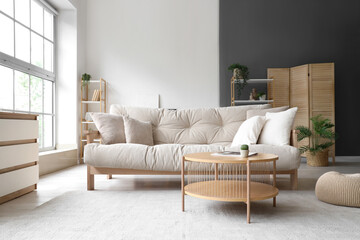 Interior of light living room with beige couch, table and shelf units