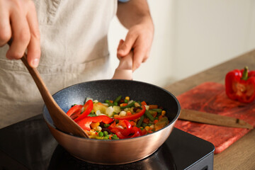 Young man frying vegetables in kitchen, closeup