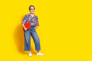 Fototapeta premium Full length photo of lovely senior lady hold netbook look empty space dressed stylish colorful garment isolated on yellow color background