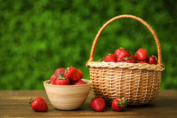 Bowl and wicker basket with sweet fresh strawberries on wooden table outdoors