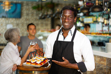 Professional friendly african american waiter holding serving tray for restaurant guests - Powered by Adobe