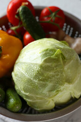 Metal colander with different wet vegetables on white textured table, above view