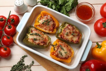 Tasty stuffed peppers in dish and ingredients on wooden table, flat lay