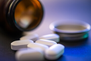 White Pills Scattered Near Open Bottle on Blue Surface, Shallow Focus on Foreground Pills