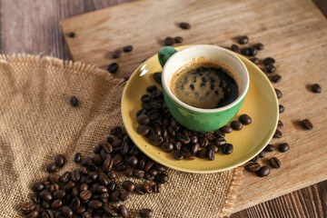 Hot coffee in green cup with coffee beans on old wooden background. Morning breakfast.