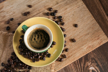 Hot coffee in green cup with coffee beans on old wooden background. Morning breakfast.