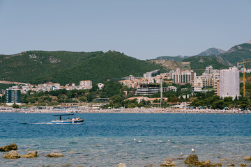 Pleasure boat sails on the sea past the resort town at the foot of the mountains