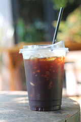 Iced americano coffee in plastic cup on wood table with nature background