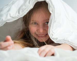 Portrait of a cute little girl laughing and hiding under the blanket. 