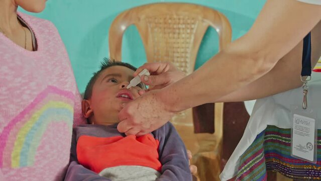 Close-up shot of a nurse administering a drinkable dose of vaccine to a Latino child.