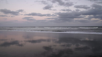 Obraz premium Panorama view of the ocean waves and beach under a sunset sky. The landscape reflection in the water.