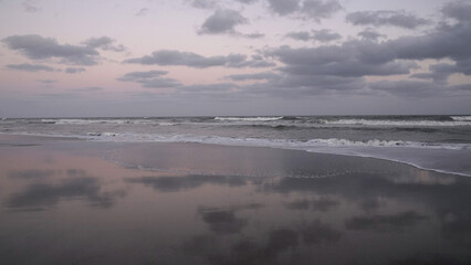 Panorama view of the ocean waves and beach under a sunset sky. The landscape reflection in the water.