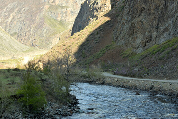 The shadow of the mountain from the setting sun covers the bed of a wide, turbulent river flowing along the bottom of a deep canyon.