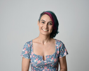 a close up head and shoulders portrait of young alternative female model, with pink and grey shaved undercut hair style, wearing a floral blue top. dramatically pulling expressive facial expressions. 